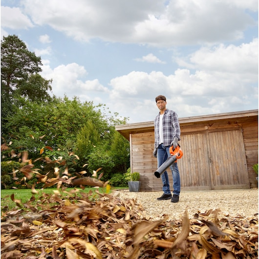 Photo of BLACKDECKER BCBL200L40 leaf blower in use, blowing leaves on a gravel driveway outdoors.