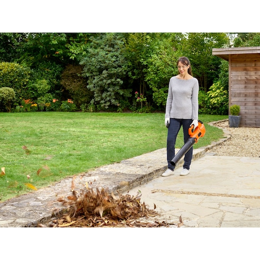 Photo of BLACKDECKER BCBL200L40 leaf blower in use clearing leaves from a patio in a garden setting.