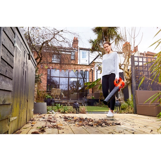 Person using BLACKDECKER BCBL200L40 cordless leaf blower on wooden deck with dry leaves in a garden.