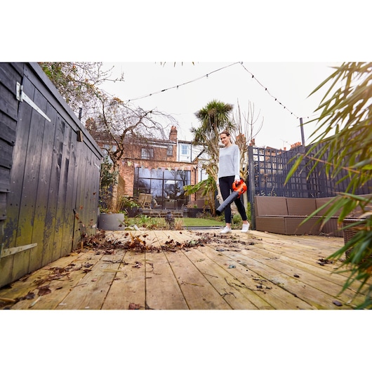 BLACKDECKER BCBL200L40 leaf blower used outdoors on wooden patio, person clearing fallen leaves near garden furniture