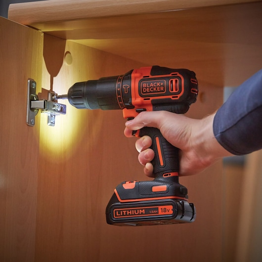 BLACK+DECKER BCD700S2AFC cordless drill with 18V lithium battery used to install hinge on wooden cabinet.