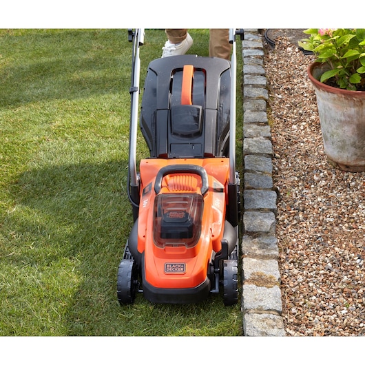 Photo of BLACKDECKER BCMW3336L1 lawn mower cutting grass near stone border in garden.