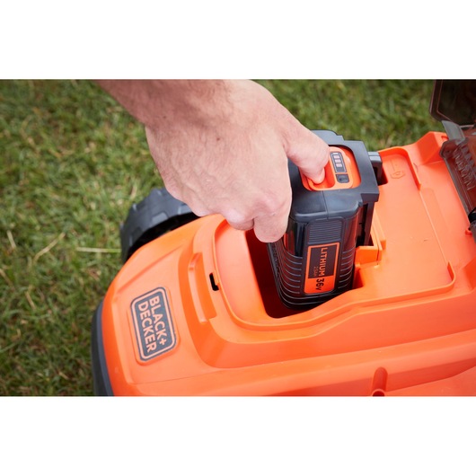 Photo of BLACK+DECKER BCMW3336L1 lawn mower battery being inserted into the orange mower body.