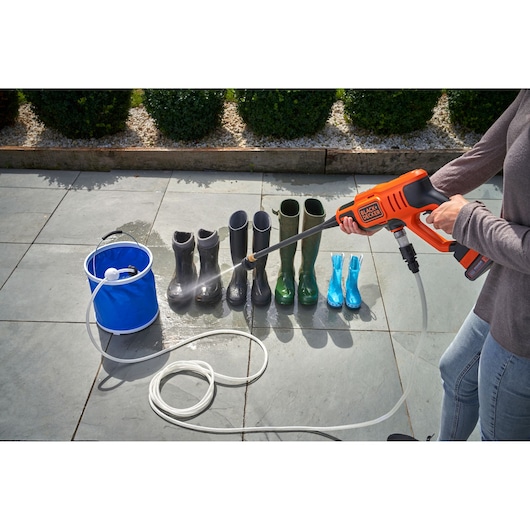 BLACK+DECKER BCPC18D1 portable pressure washer spraying water on boots outdoors, blue bucket visible, side angle.