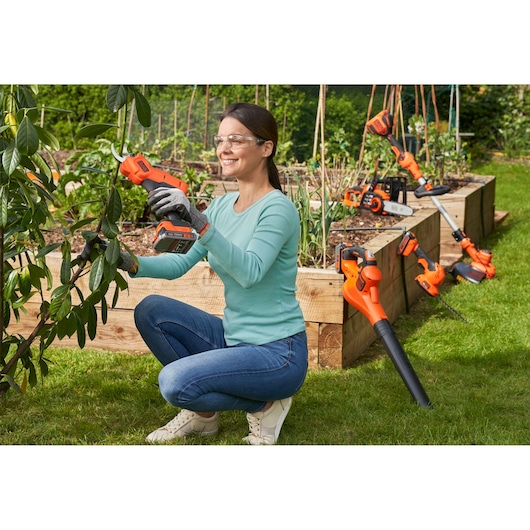 BLACKDECKER BCPP18D1 cordless garden pruner used by person near raised garden beds outdoors.