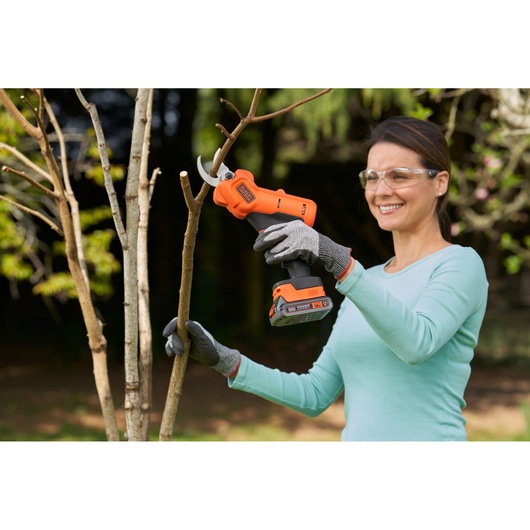 BLACKDECKER BCPP18D1 cordless pruning shears shown cutting tree branch outdoors.