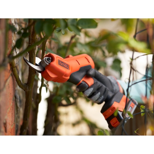 BLACK+DECKER BCPP18D1 cordless electric pruner in use trimming outdoor plant stems, close-up.