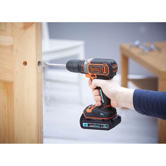 BLACKDECKER BDCDC18KST cordless drill used to bore hole in wooden door, close-up side angle.