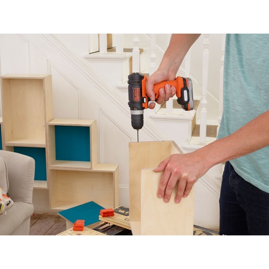 Photo of BLACKDECKER BDCDD12USB cordless drill in use, drilling wood for furniture assembly indoors.