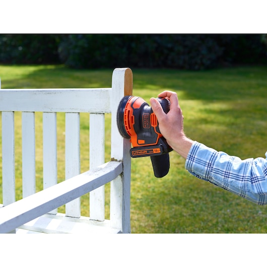 BLACKDECKER BDCROS18N cordless random orbit sander being used to sand a white wooden chair outdoors.