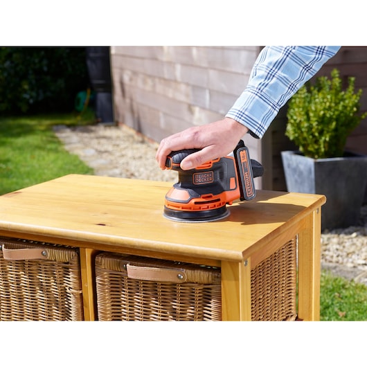 BLACKDECKER BDCROS18N cordless sander used on wooden cabinet outdoors.