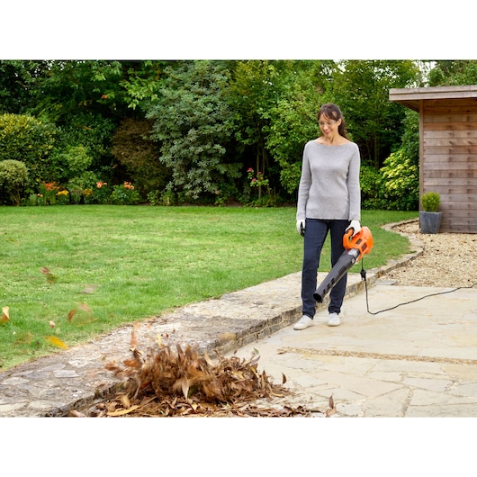 BLACKDECKER BEBL185 leaf blower in use clearing leaves on patio in garden setting.