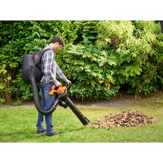 BLACKDECKER BEBLV230 garden vacuum with backpack in use collecting leaves on grass.