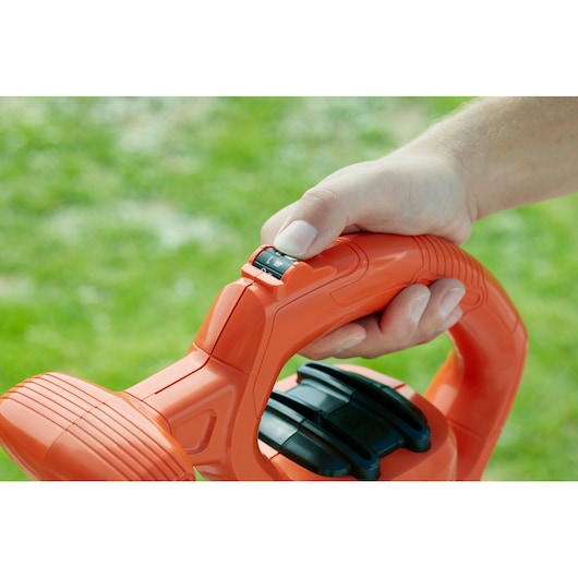 Close-up of hand adjusting speed switch on BLACKDECKER BEBLV230 orange garden tool handle outdoors.