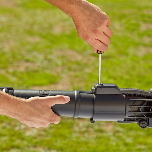 Photo of hands assembling BLACKDECKER BEBLV230 lawn tool tube using a screwdriver outdoors.