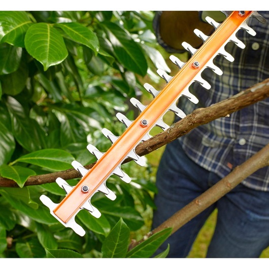 BLACKDECKER BEHT201 hedge trimmer cutting a thick branch in a garden, close-up view.