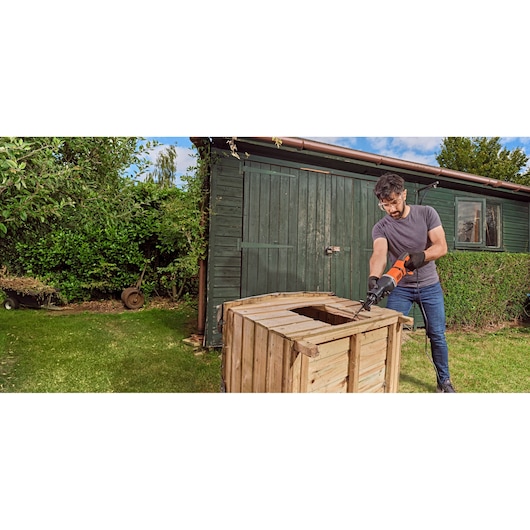 Man using BLACK+DECKER BES301 reciprocating saw to cut wood outdoors next to a green shed.