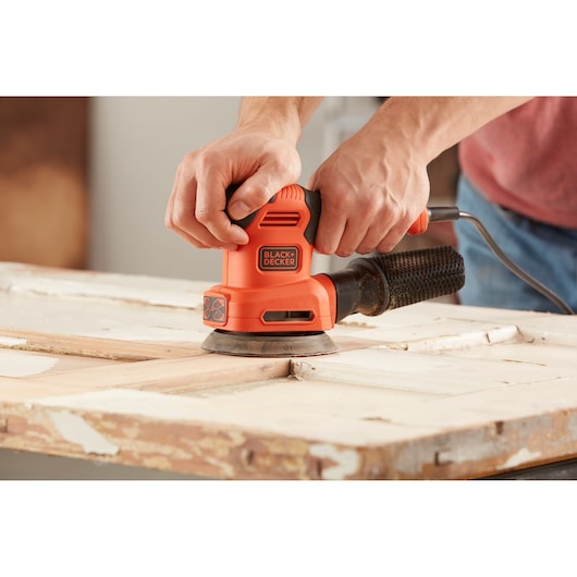 BLACKDECKER BEW200 orange electric sander used on a wooden surface, close-up view.