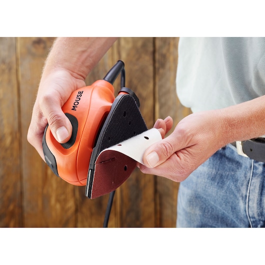 BLACKDECKER BEW230 compact orange detail sander held in hand, sanding sheet being attached.
