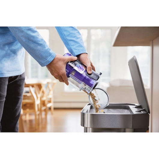 BLACKDECKER BHFEA640WG vacuum dustbin being emptied into a trash can in a bright kitchen setting.