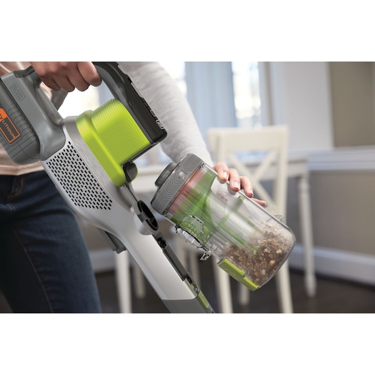 Photo of BLACKDECKER BHFEV362DA cordless vacuum with green accents, showing dust container being emptied in a home setting.