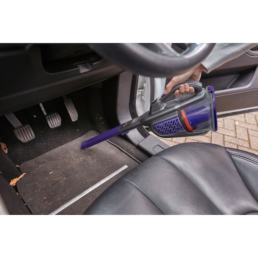 BLACK+DECKER BHHV520BFP handheld vacuum cleaning a car floor with narrow nozzle attachment.