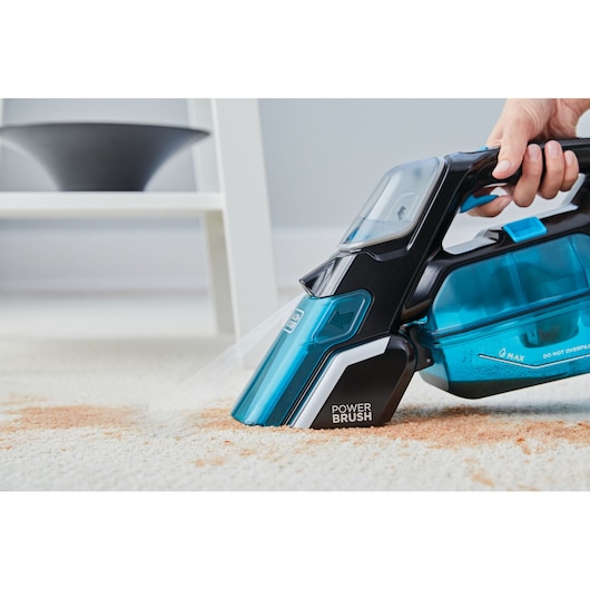 BLACK+DECKER BHSB320JP handheld carpet cleaner with visible power brush cleaning a spill on light carpet, side angle.