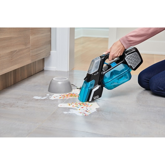 BLACK+DECKER BHSB320JP handheld vacuum cleaning spilled cereal and milk on tile floor, side view.
