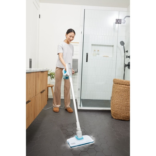 Person using BLACK+DECKER BHSM15FX08 steam mop on hexagonal tile bathroom floor near shower.