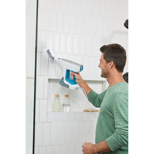 BLACKDECKER BHSM15FX08 handheld steam cleaner used on white tiled bathroom wall.