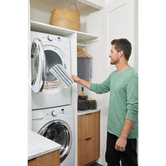 BLACKDECKER BHSM15FX08 mop pad held by person near stacked laundry machines in home laundry room.