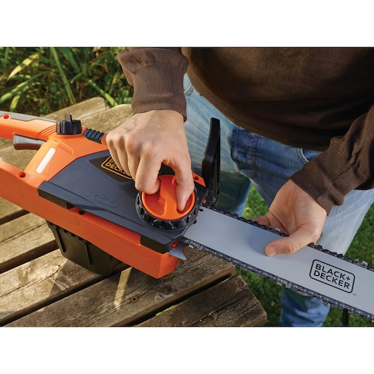 Photo of BLACK+DECKER CS2245 chainsaw being adjusted by hand, showing chain tension knob and blade close-up.
