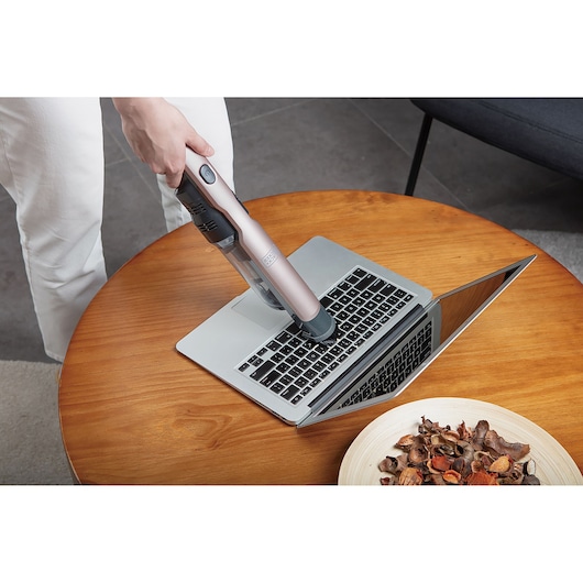 BLACK+DECKER DVC320BRG handheld vacuum cleaning laptop keyboard on wooden table.