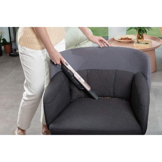 BLACKDECKER DVC320BRG handheld vacuum cleaning crumbs from a dark armchair in a living room scene.