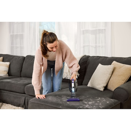 BLACKDECKER DVD320BP handheld vacuum cleaning pet hair from a dark gray sofa in a living room.