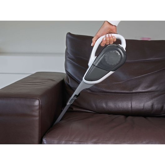 A BLACK+DECKER handheld vacuum cleaner being used to clean between the cushions of a dark brown leather sofa.