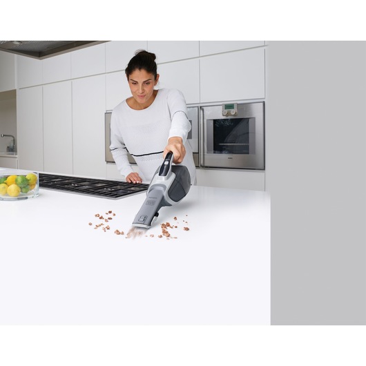 BLACKDECKER DVJ320JG handheld vacuum in use cleaning crumbs on white kitchen counter.