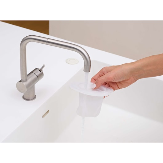 BLACKDECKER DVJ320JG vacuum filter being rinsed under faucet in a white sink, close-up angle.