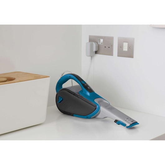 Photo of BLACK+DECKER DVJ320J handheld vacuum cleaner in blue and gray, charging on a white countertop.
