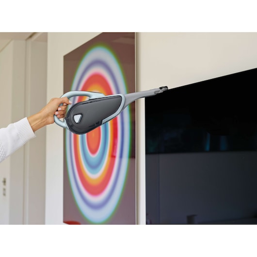 BLACKDECKER DVJ325J handheld vacuum cleaner with long nozzle used to clean a TV screen indoors.