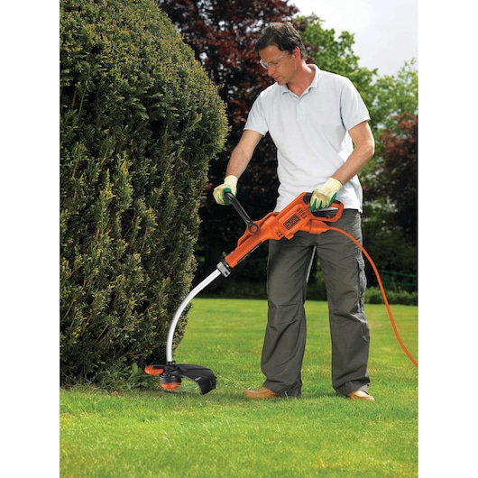 BLACKDECKER GL933 orange corded grass trimmer used outdoors with curved shaft and black trim.