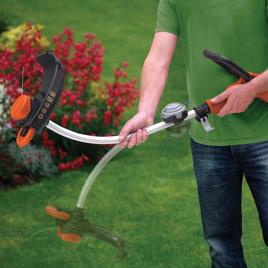 BLACK+DECKER GL933 grass trimmer with curved shaft held by person in garden with red flowers.