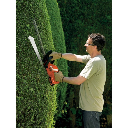 Photo of a person using BLACK+DECKER GTC1845L20 cordless hedge trimmer on a green hedge outdoors.