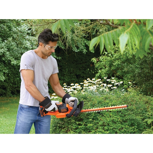 Photo of BLACKDECKER GTC18502PC hedge trimmer in use trimming bushes in a garden.