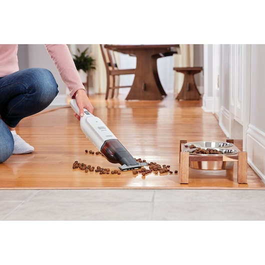 BLACKDECKER HLVC315J11 handheld vacuum cleaning pet food from wooden floor near pet bowls.