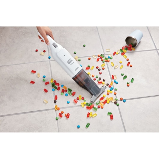 BLACKDECKER HLVC315J11 handheld vacuum cleaning colorful candy from tile floor, top angle.