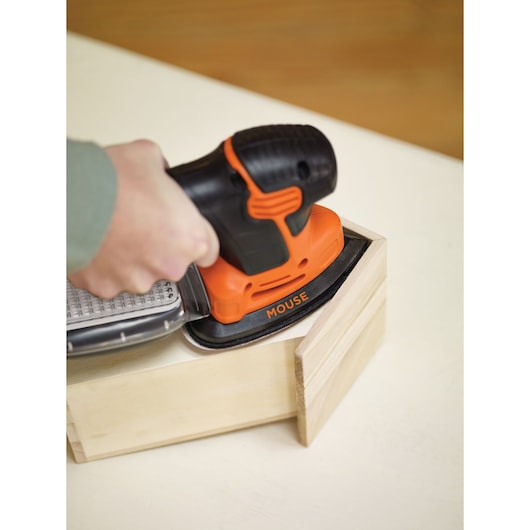 BLACKDECKER KA2000KA10 orange and black mouse sander in use on a wooden box, close-up angle.