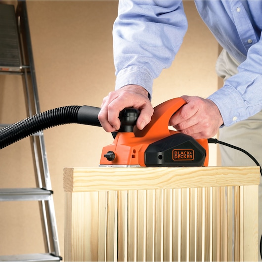 BLACK+DECKER KW712 electric planer in use on wood, showing vacuum attachment, close-up side view.