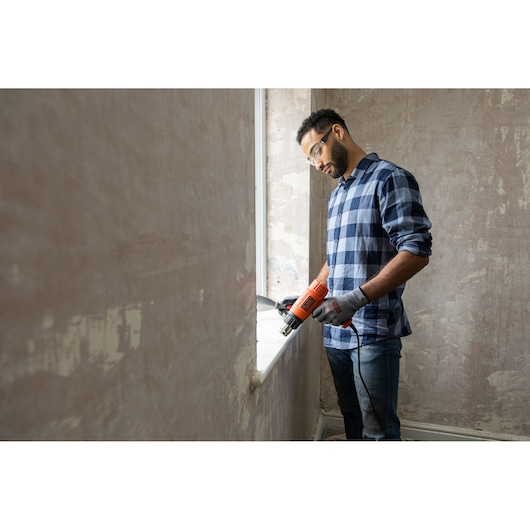 Photo of BLACKDECKER KX1650A heat gun used for window renovation, held by person in gloves and plaid shirt.