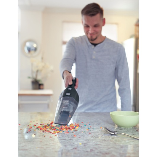 BLACKDECKER NSVA315J handheld vacuum cleaning colorful crumbs from kitchen counter near green bowl.